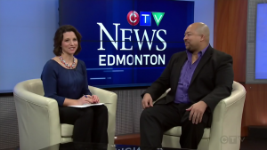 Two individuals sit in a studio set for CTV News Edmonton during an interview, with a news screen in the background.